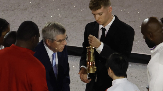 El presidente del COI, Thomas Bach (izq.), y el nadador francés Leon Marchand apagan la llama olímpica.